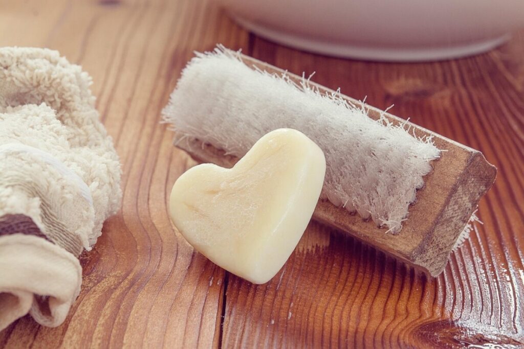 Cream soap bar beside a wooden scrub brush and towel
