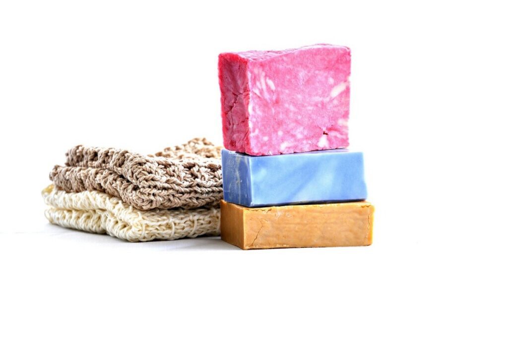 Pink, blue and ochre soap bars stacked beside crocheted washcloths