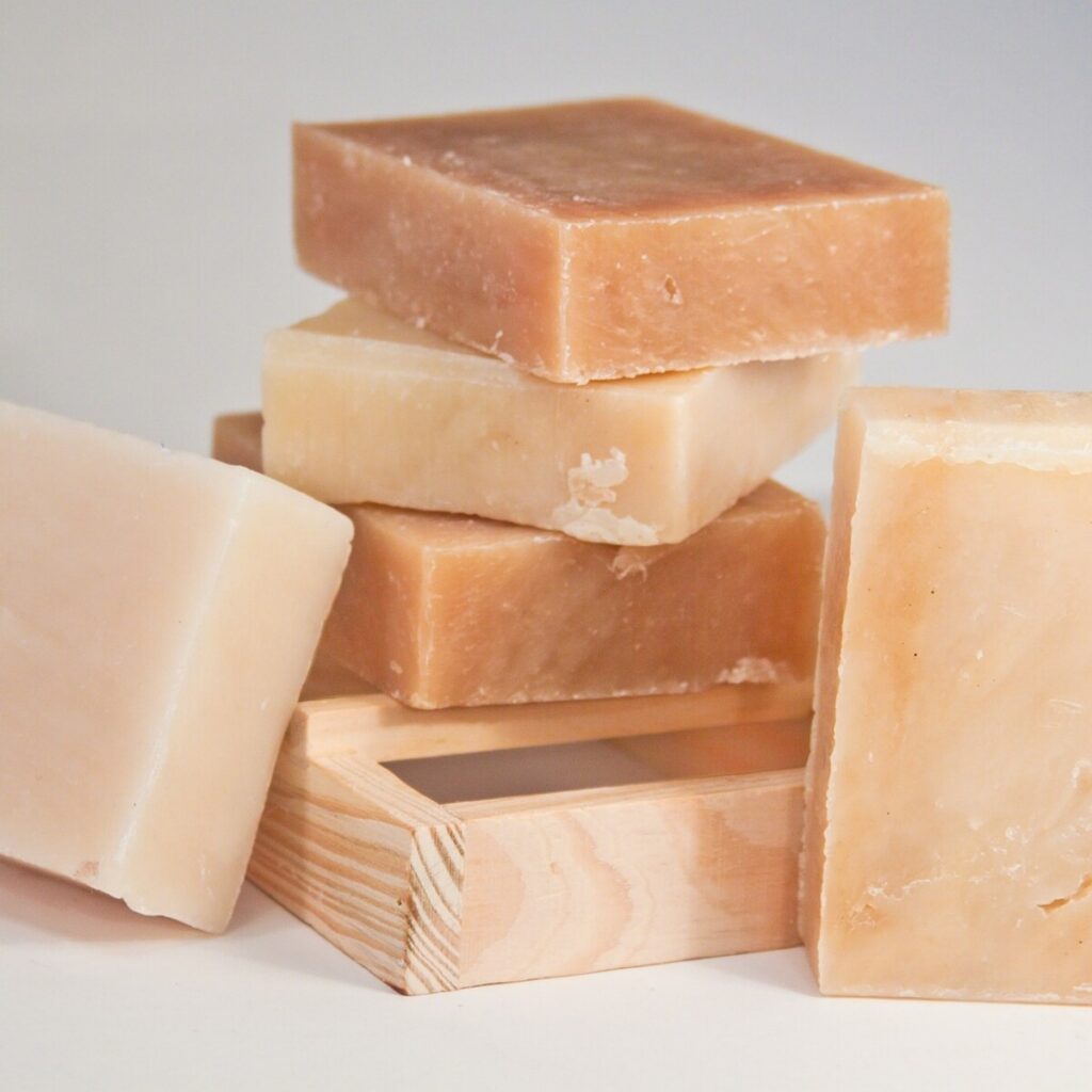 Stack of plain cream and tan soap bars with a wooden soap dish