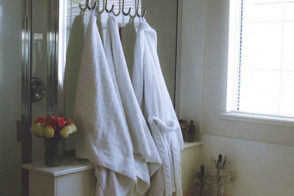 White towels and a bathrobe hanging on hooks in a bright bathroom