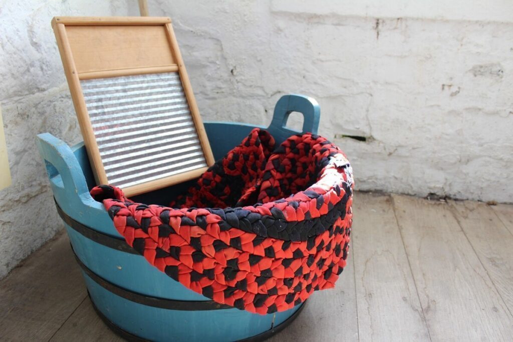 Washboard and blue wooden tub with a red and black rag rug