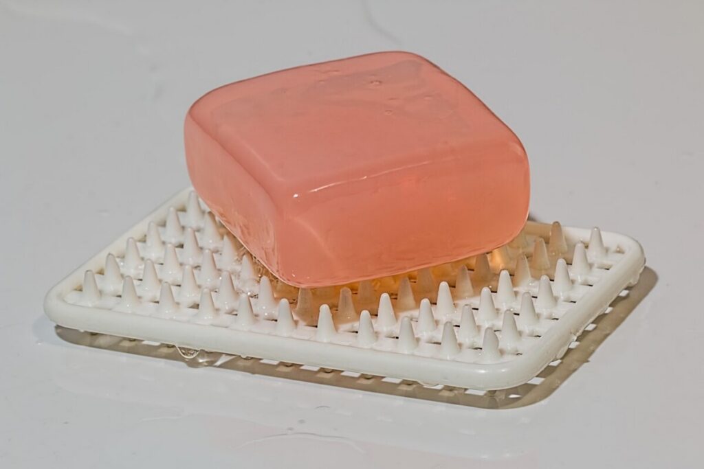 Pink soap bar resting on a white draining soap dish
